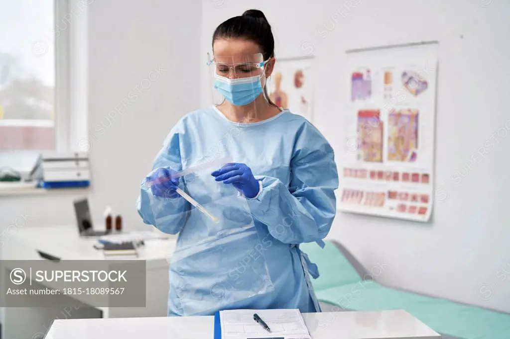 Mature female doctor with face shield putting medical sample in zipper bag