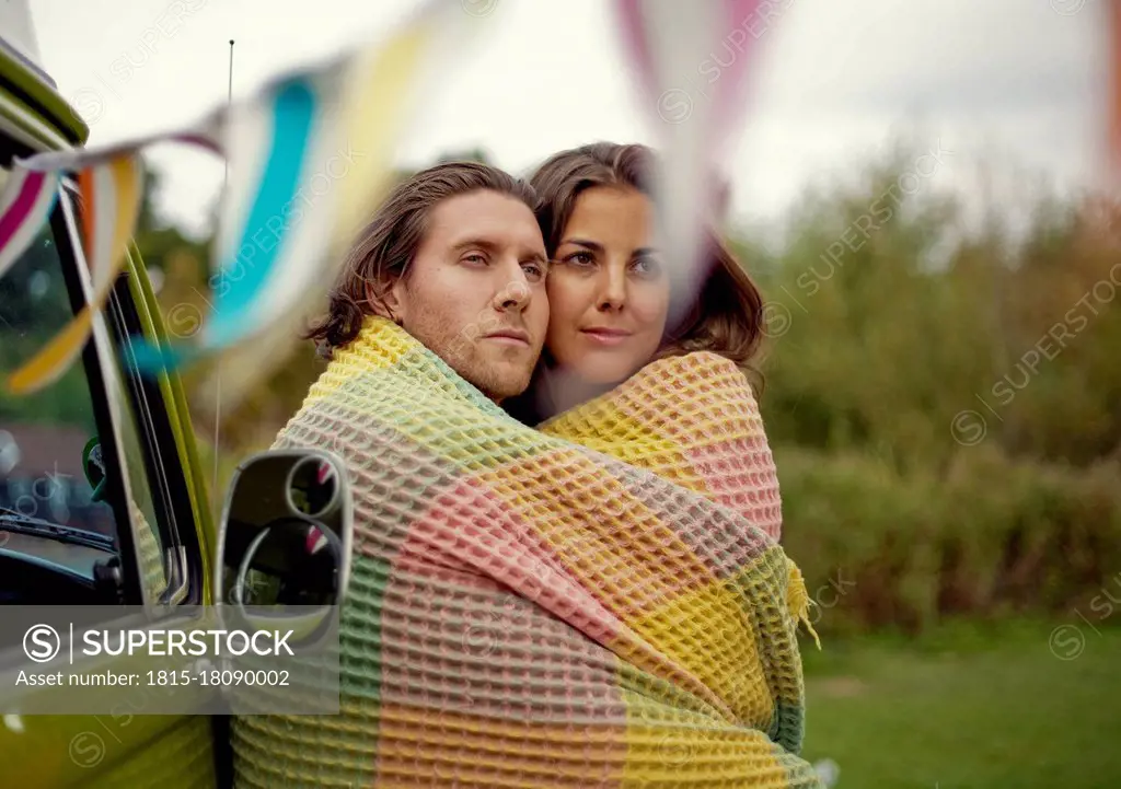 Young man and woman wrapped in blanket embracing each other