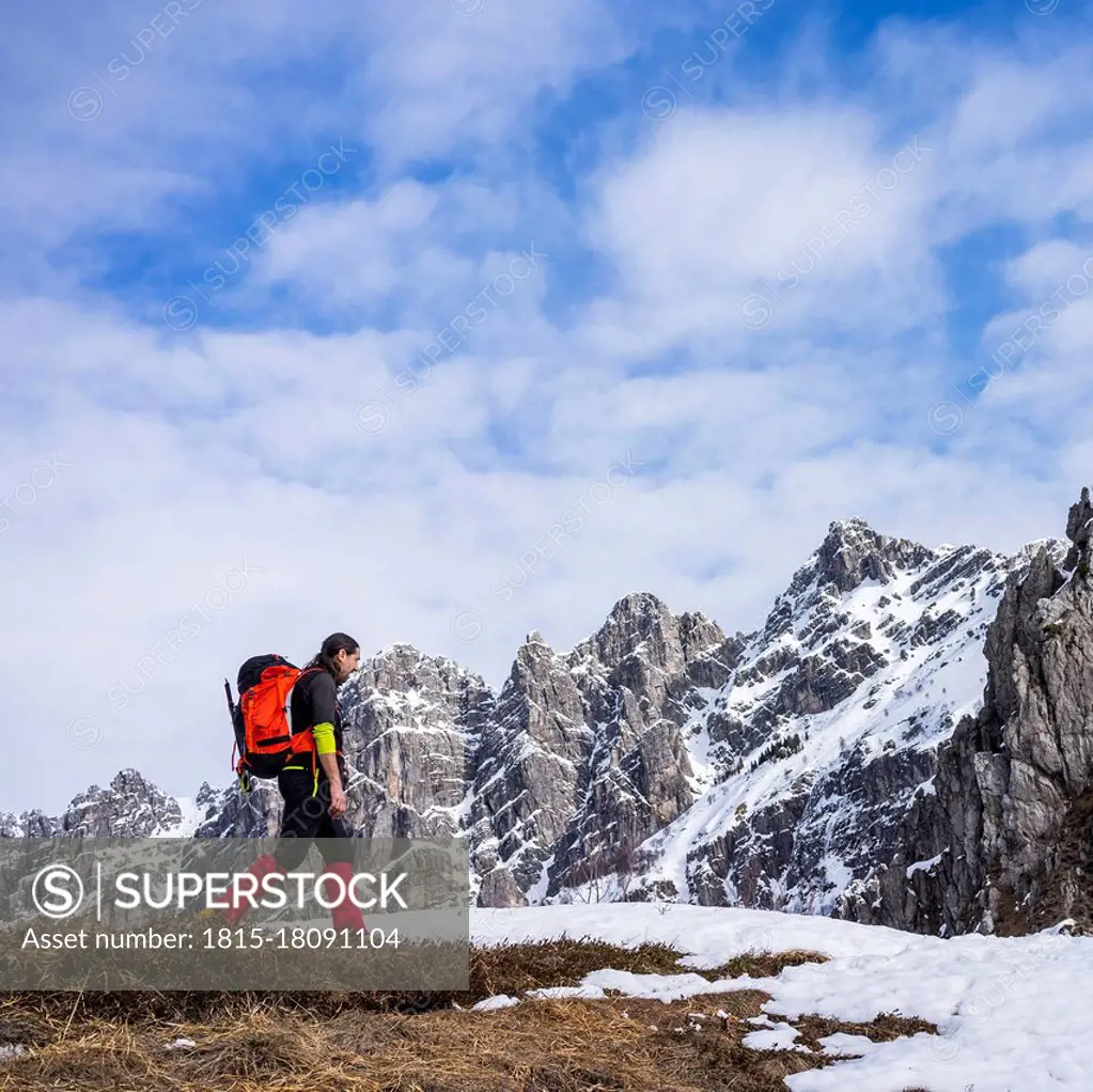 Man hiking on snowcapped mountain against cloudy sky