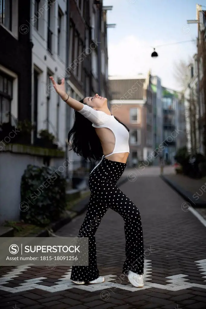 Woman dancing with arms outstretched on footpath at street