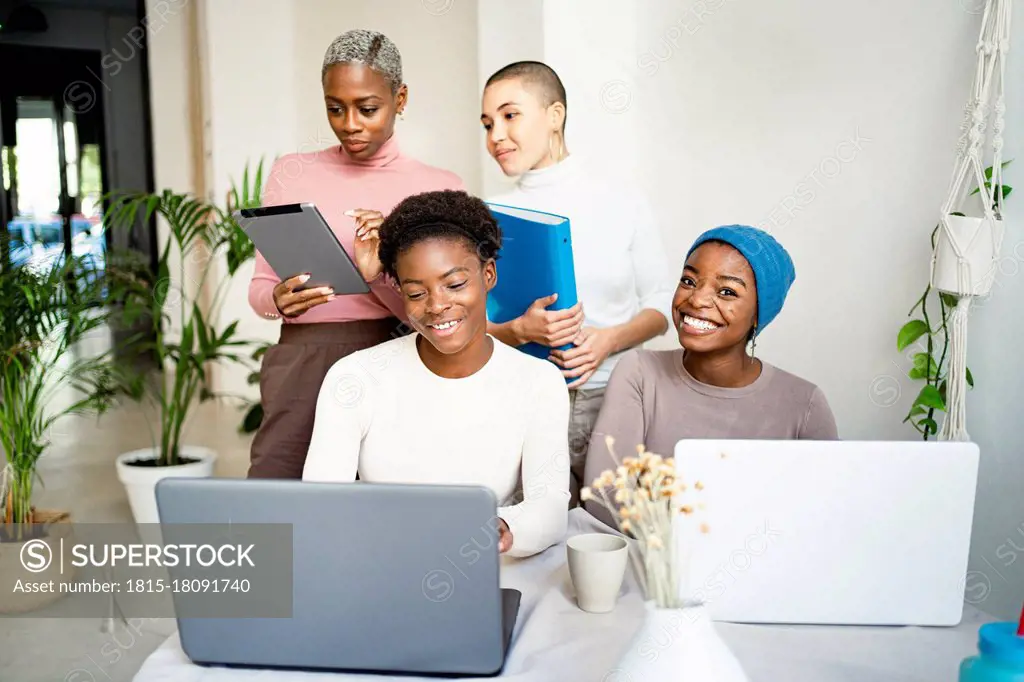 Happy female colleagues working on laptop at home