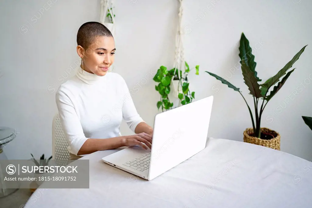 Smiling young female entrepreneur using laptop while working at home