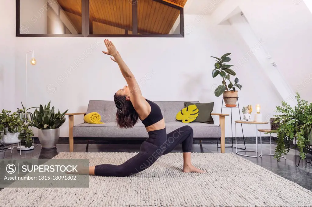 Woman practicing Yoga pose against sofa in living room at home