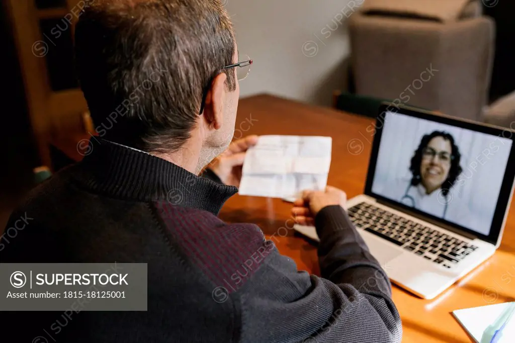 Senior male holding prescription while consultation on video call to female doctor at home during COVID-19