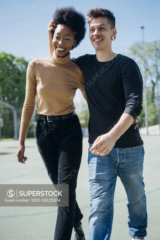 Cheerful couple walking at sports court during sunny day