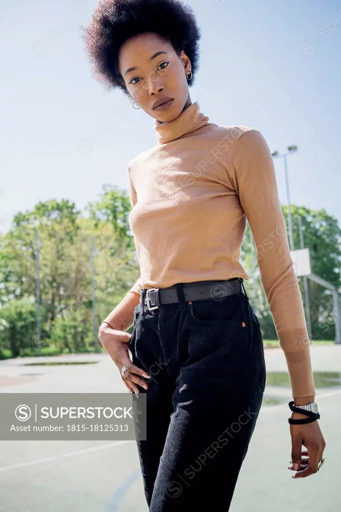 Young woman standing with hand in pocket at sports court during sunny day