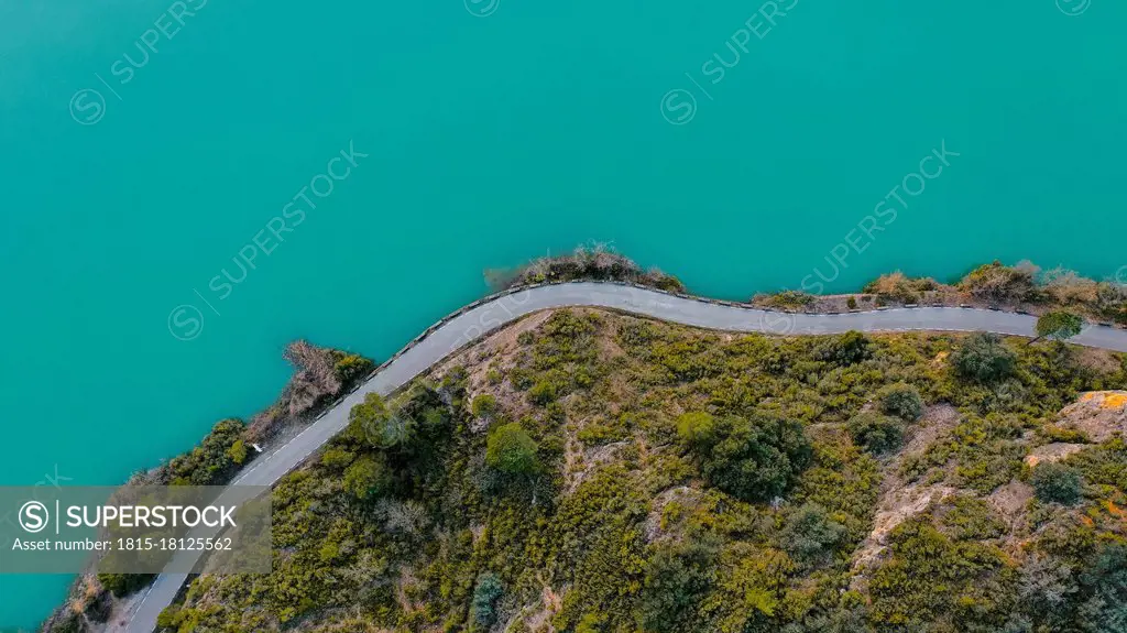 Aerial view of country road stretching along shore of turquoise lake