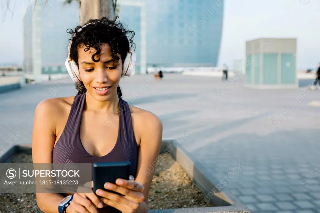 Female athlete with headphone using mobile phone in city