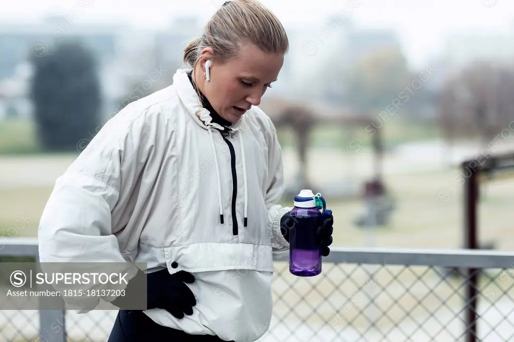 Exhausted female athlete drinking water after exercising in park