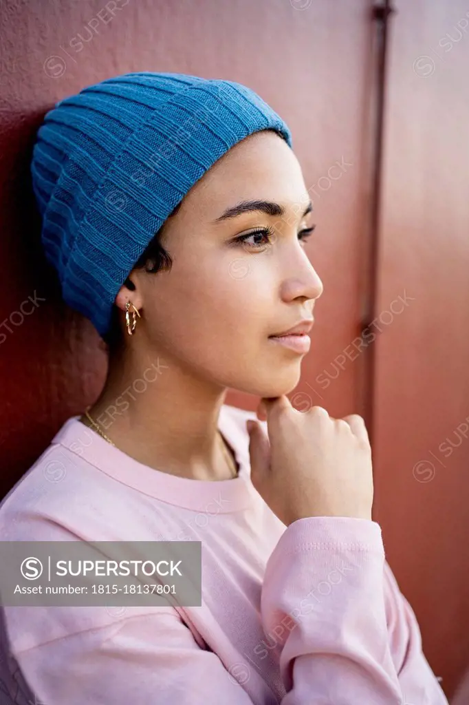 Beautiful woman with hand on chin day dreaming in front of wall