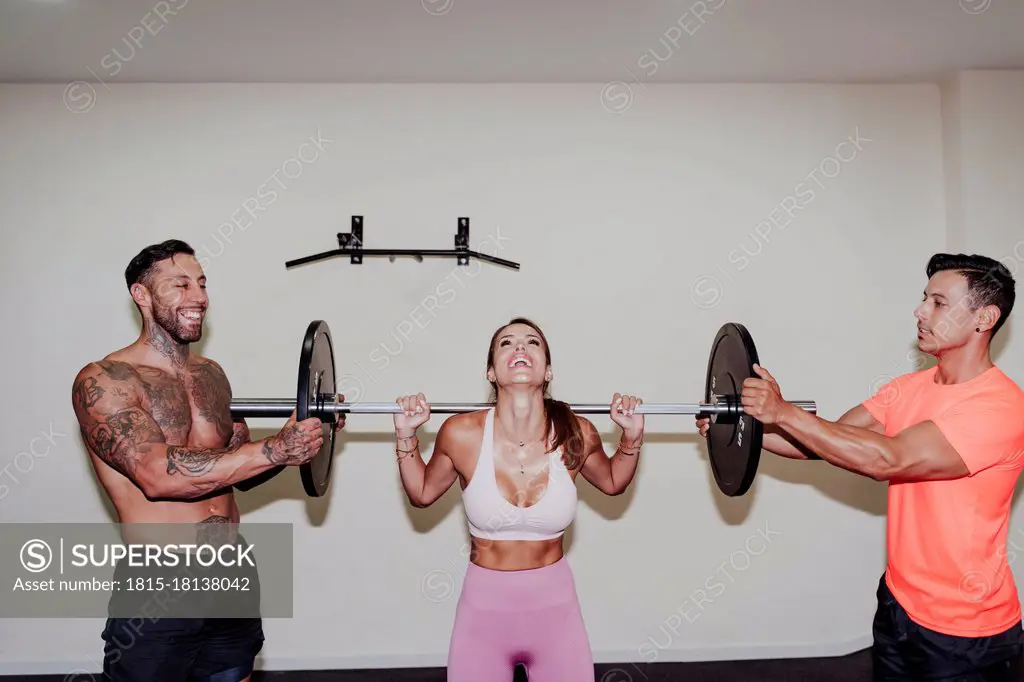 Male athletes helping female friend in exercising with barbell at gym