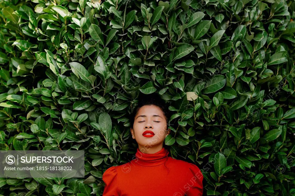 Woman with eyes closed in front of green plants