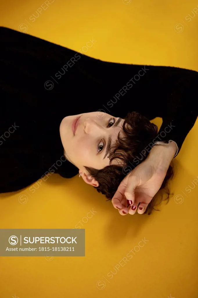 Young woman staring while lying on yellow background