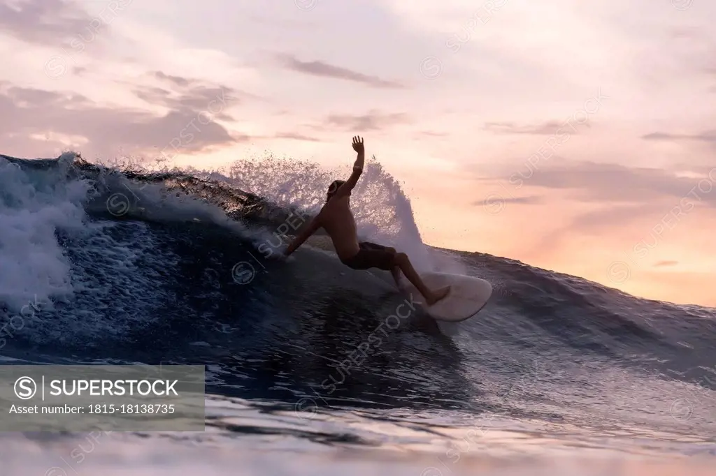 Tourist surfing over waves in sea during sunset