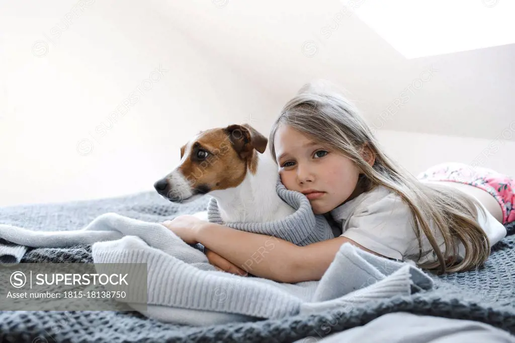 Cute girl embracing dog while lying on bed at home