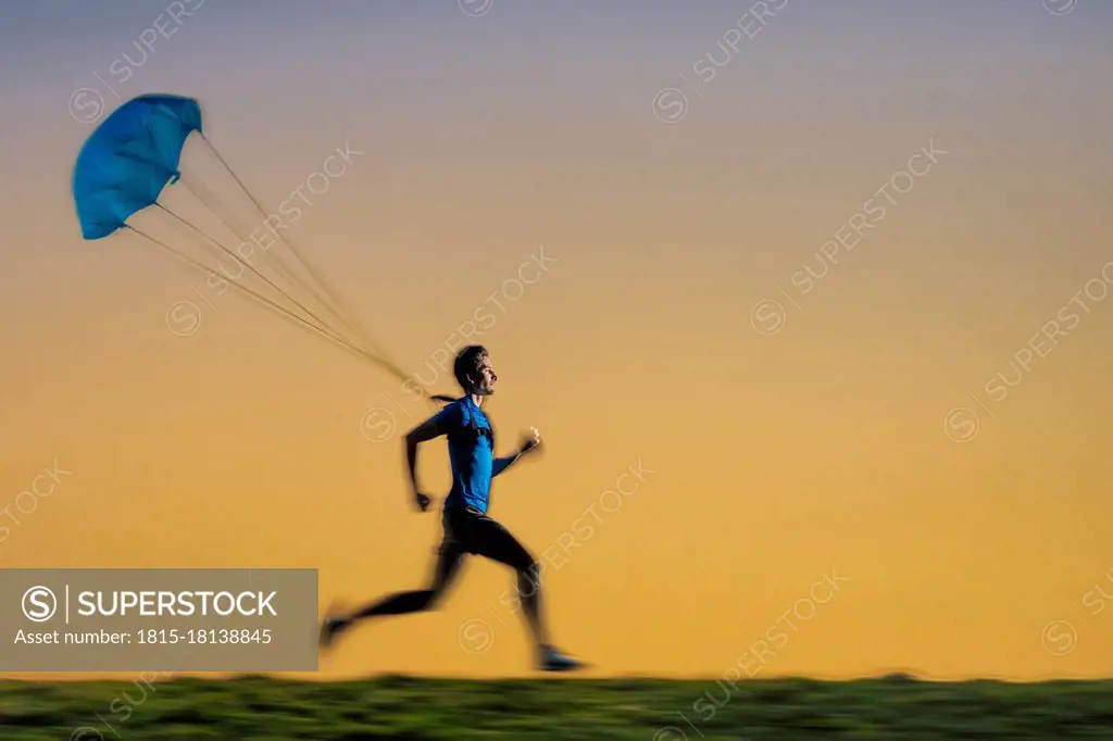 Male sportsperson jogging with parachute during sunset