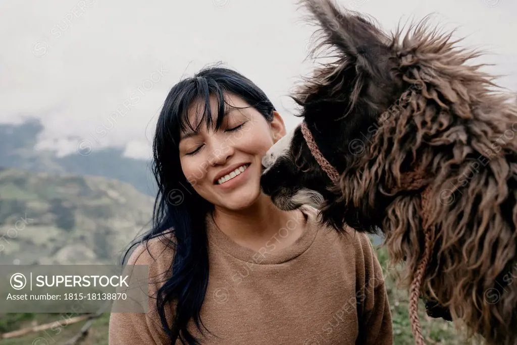 Smiling woman with eyes closed standing by Alpaca