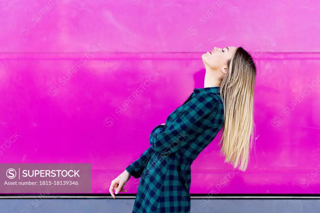 Young woman with head back standing by pink wall