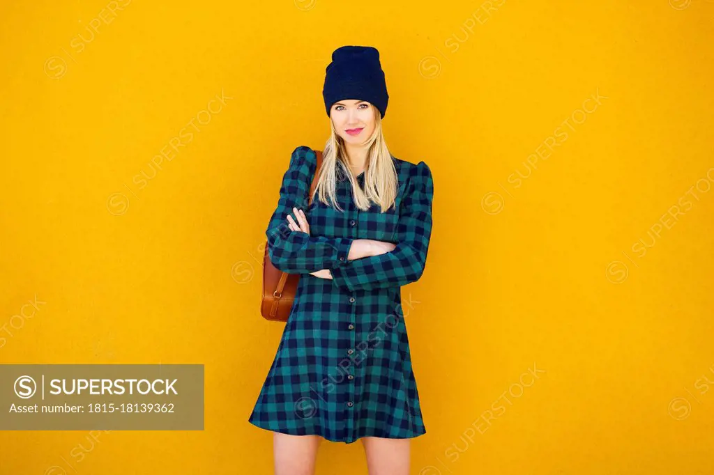 Beautiful woman with arms crossed standing in front of yellow wall