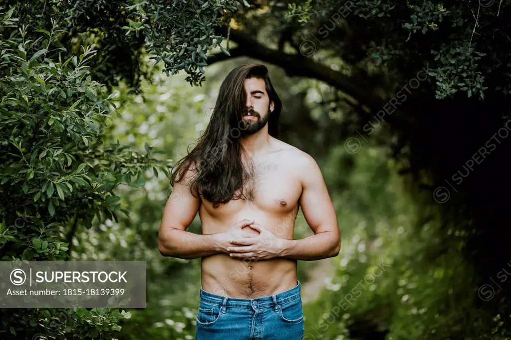 Shirtless man with eyes closed standing and relaxing in forest