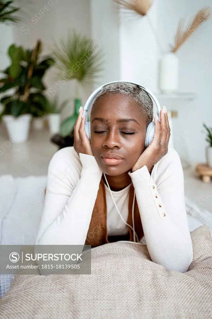 Beautiful woman with eyes closed listening music through headphones while lying at home