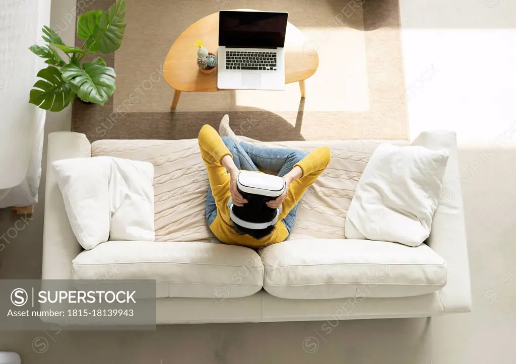 Woman holding Virtual reality headset while sitting on sofa at home