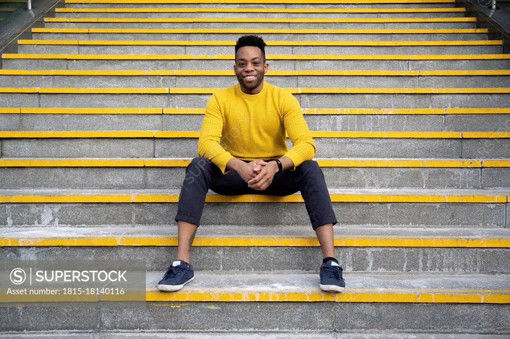 Smiling man with hands clasped sitting on staircase