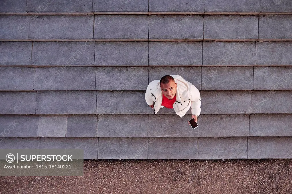 Young man holding smart phone while standing on steps