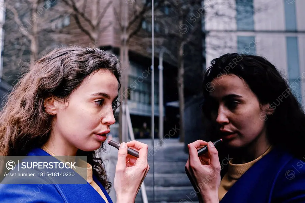 Young businesswoman applying lipstick while looking at reflection