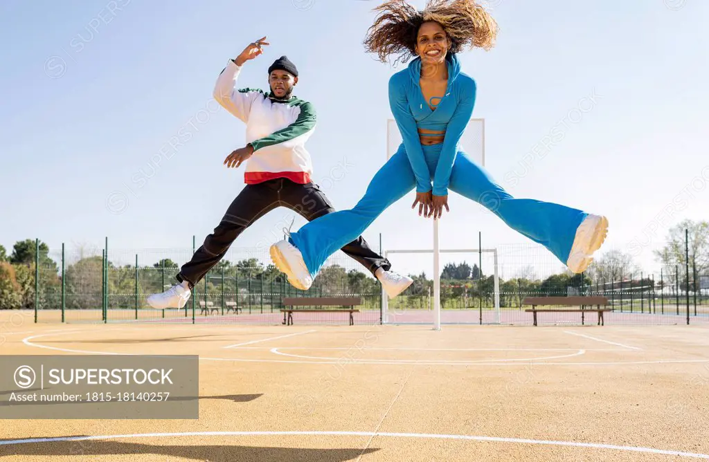 Confident male and female friends jumping while dancing on basketball court