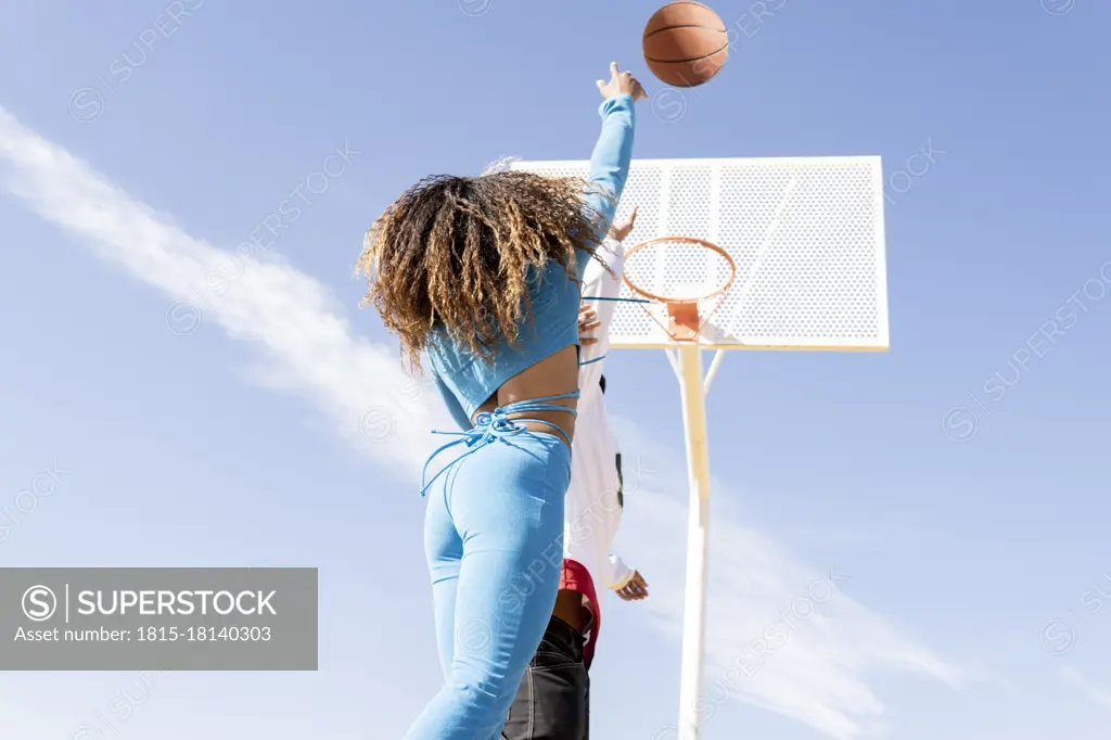 Female friend shooting in basketball hoop while playing on sports court