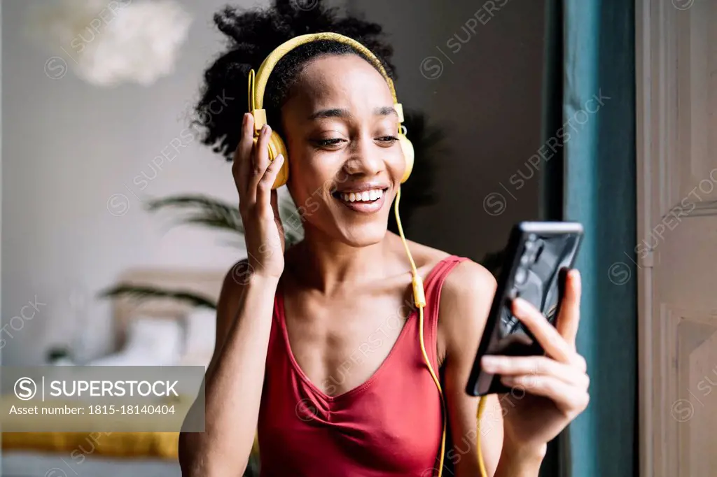 Beautiful woman touching headphones while using smart phone at home