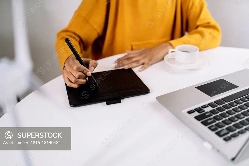 Woman using graphic tablet by laptop at home