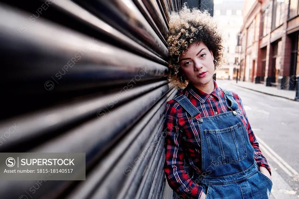 Hipster woman with hands in pockets leaning on shutter