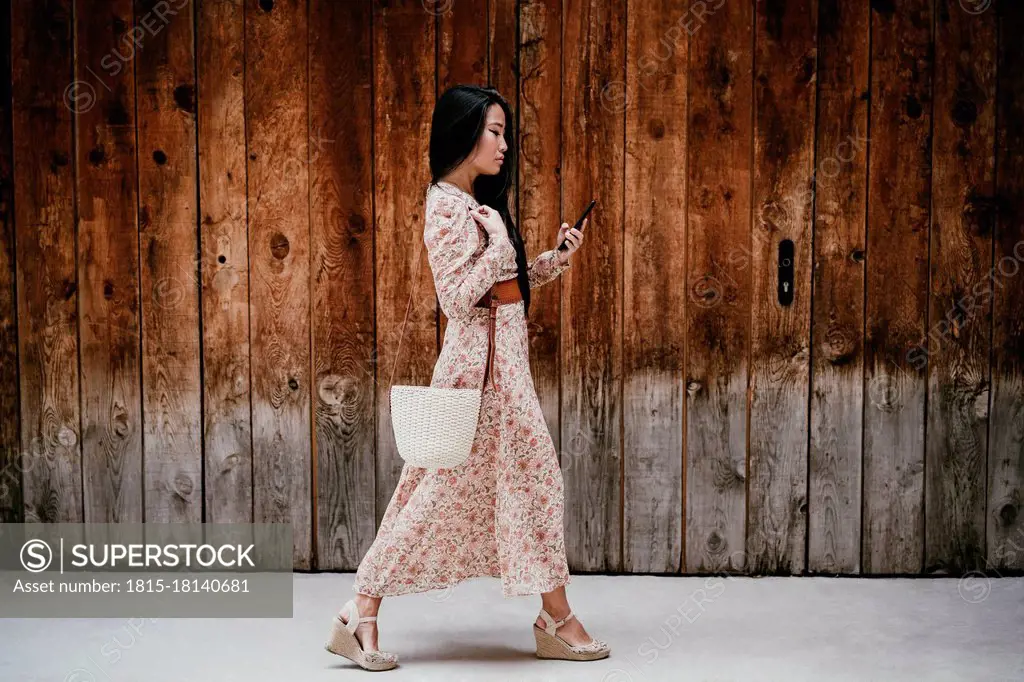 Woman using smart phone while walking by by old wooden door