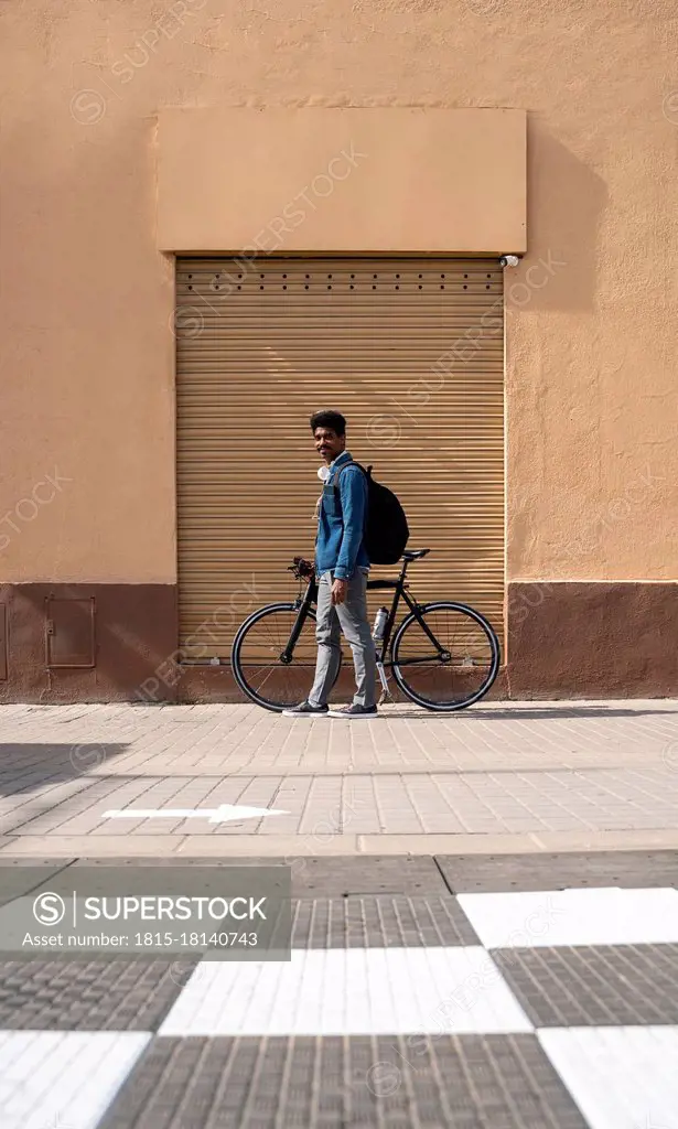 Man with bicycle standing by wall during sunny day