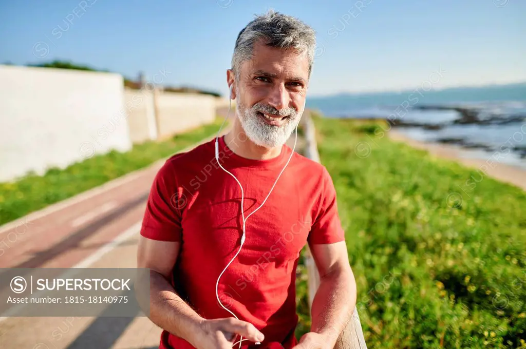 Smiling man with earphones leaning on railing by the sea