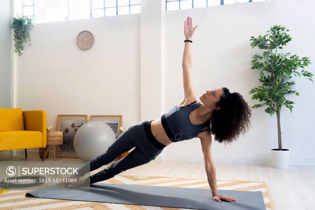 Young woman practicing side plank pose in living room