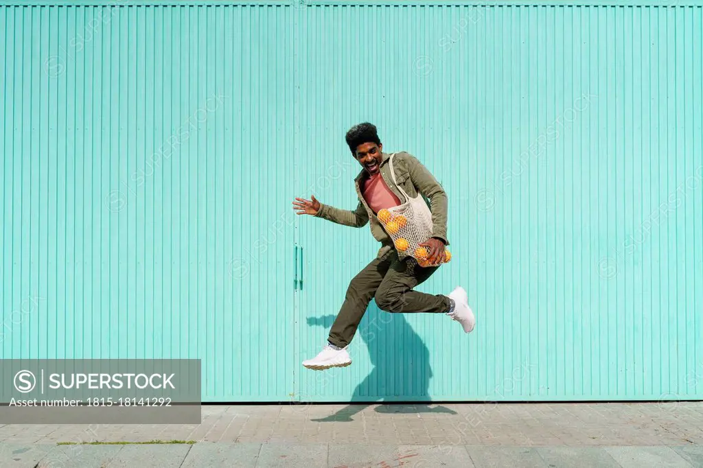 Ecstatic man dancing in front of turquoise wall during sunny day