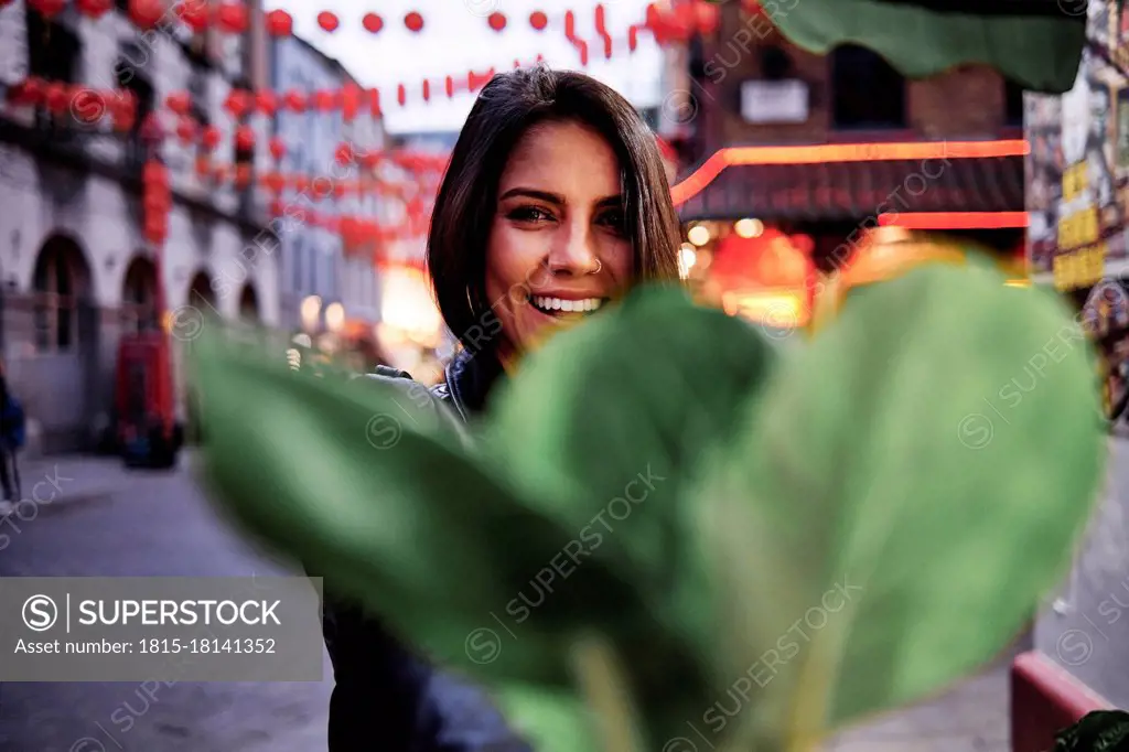 Happy young woman in front of plant in city