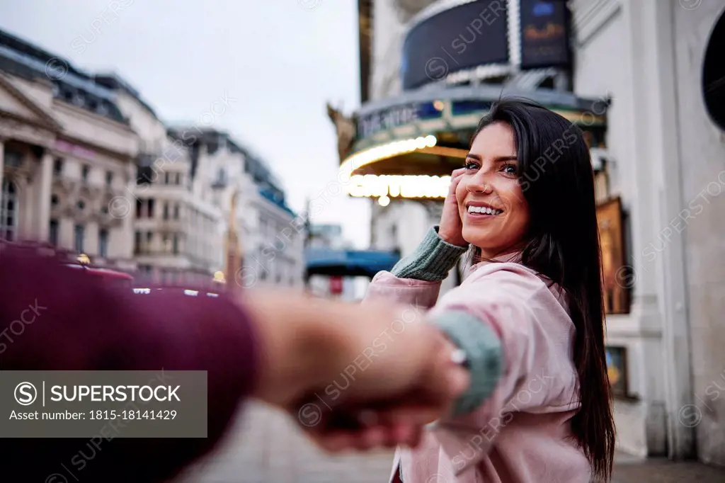 Happy young woman holding hand of boyfriend n city