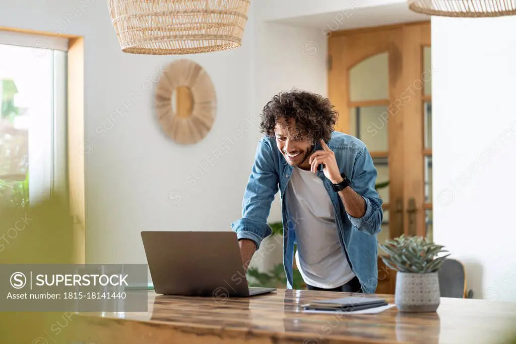 Male entrepreneur using laptop while talking on phone at home