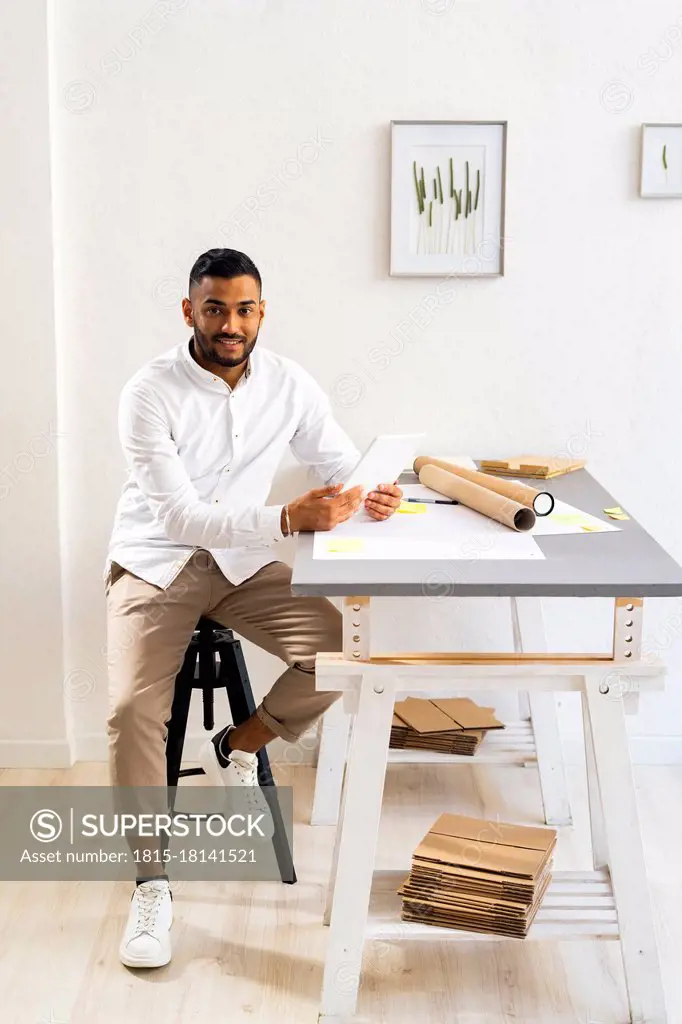 Businessman with digital tablet sitting at desk by wall in office