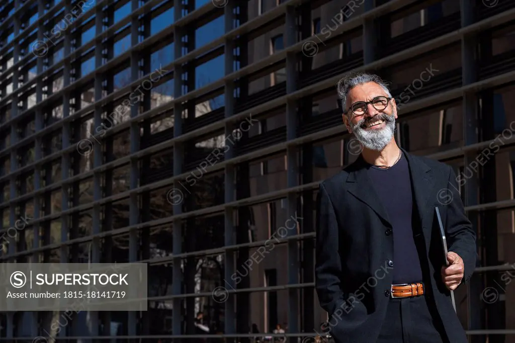 Contented businessman with laptop standing by building