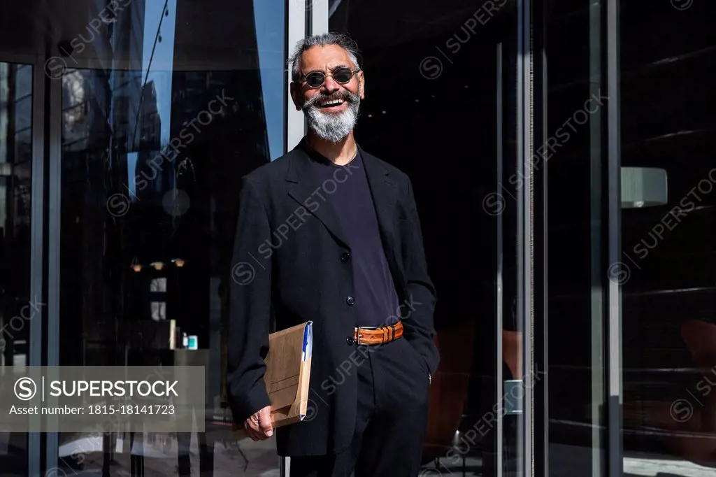 Smiling male professional with file standing by building in city