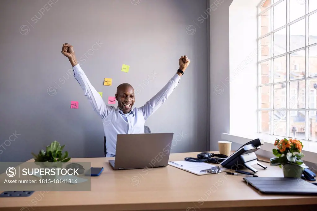 Businessman with hands raised looking at laptop on desk at office