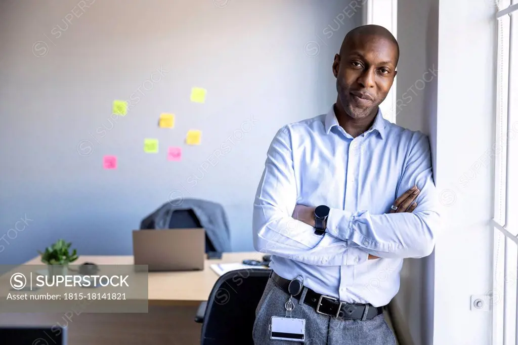 Businessman with arms crossed leaning on wall at office