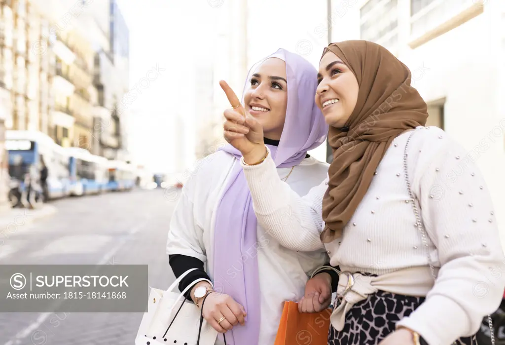 Young woman pointing to female friend while shopping in city