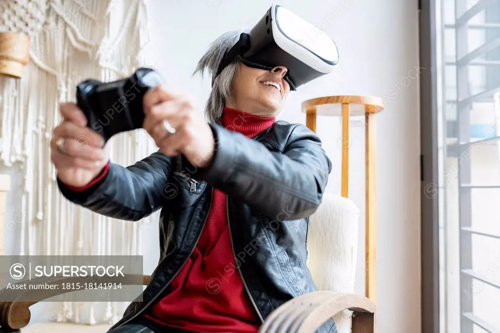 Smiling woman with game controller playing through virtual reality simulator at home