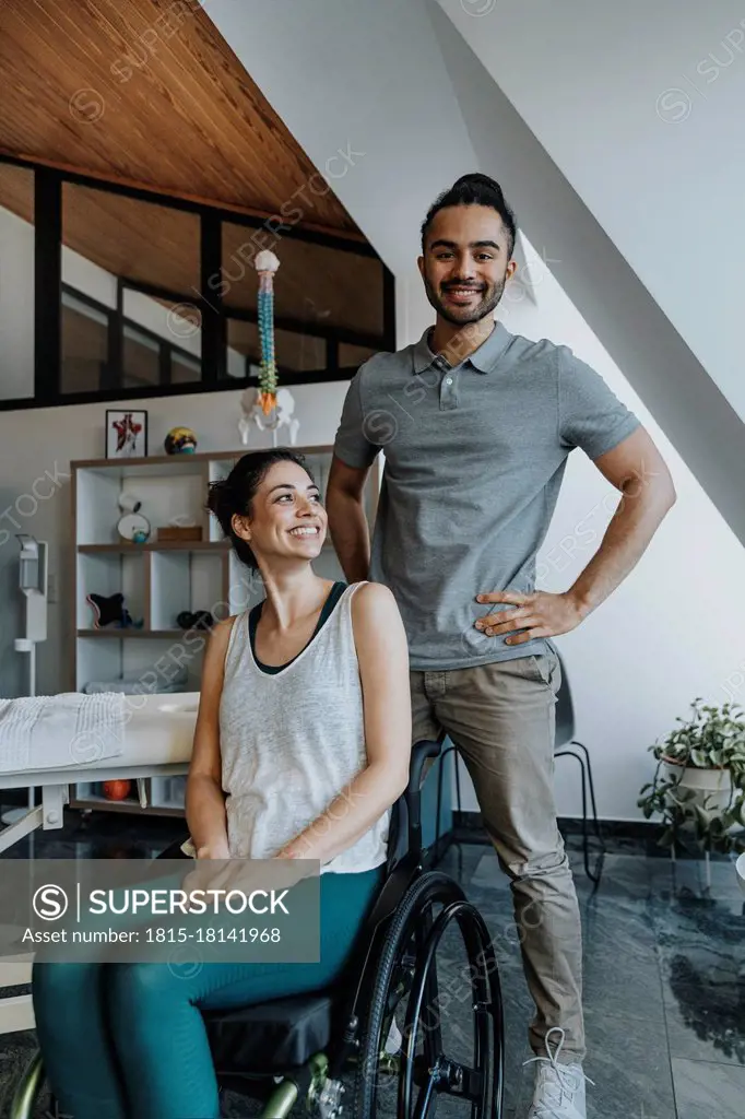 Smiling male physiotherapist standing while female patient sitting on wheelchair